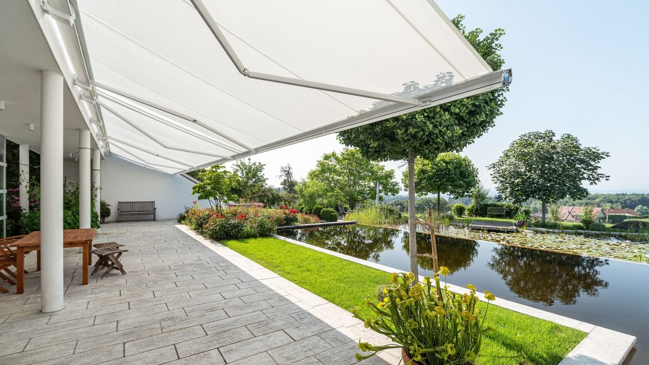 Koblede hvide Markilux 6000 kassettemarkiser over en terrasse ved en dam