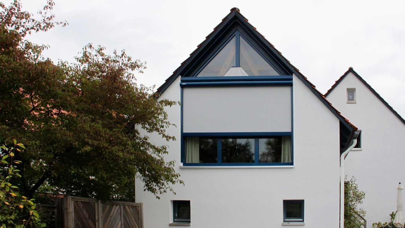 Hvidt hus med trekantet gavlvindue og halvt udstrakt Markilux 893 vinduesmarkise